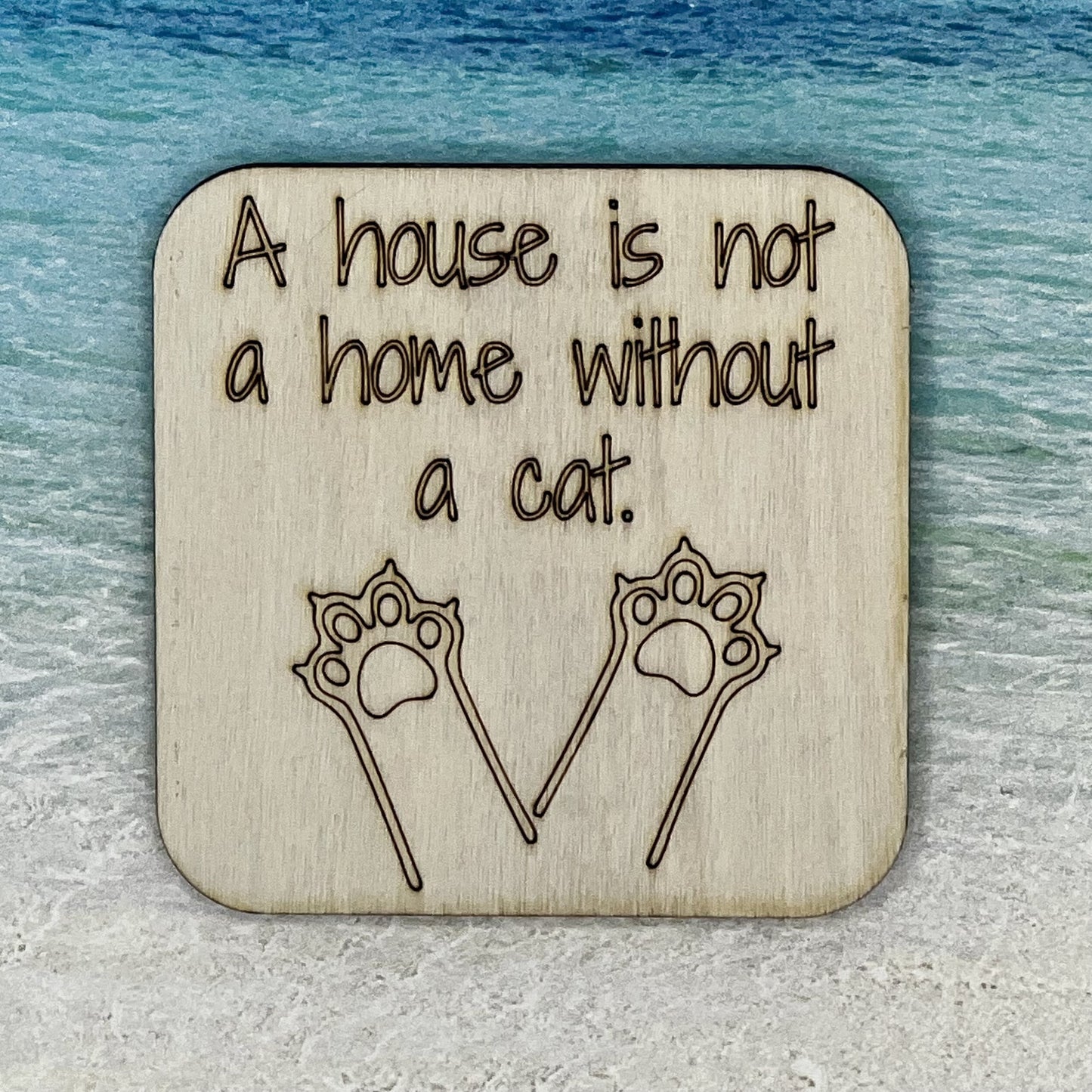 2.5" basewood square with “A house is not a home without a cat“ laser engraved text with image of cat paws.