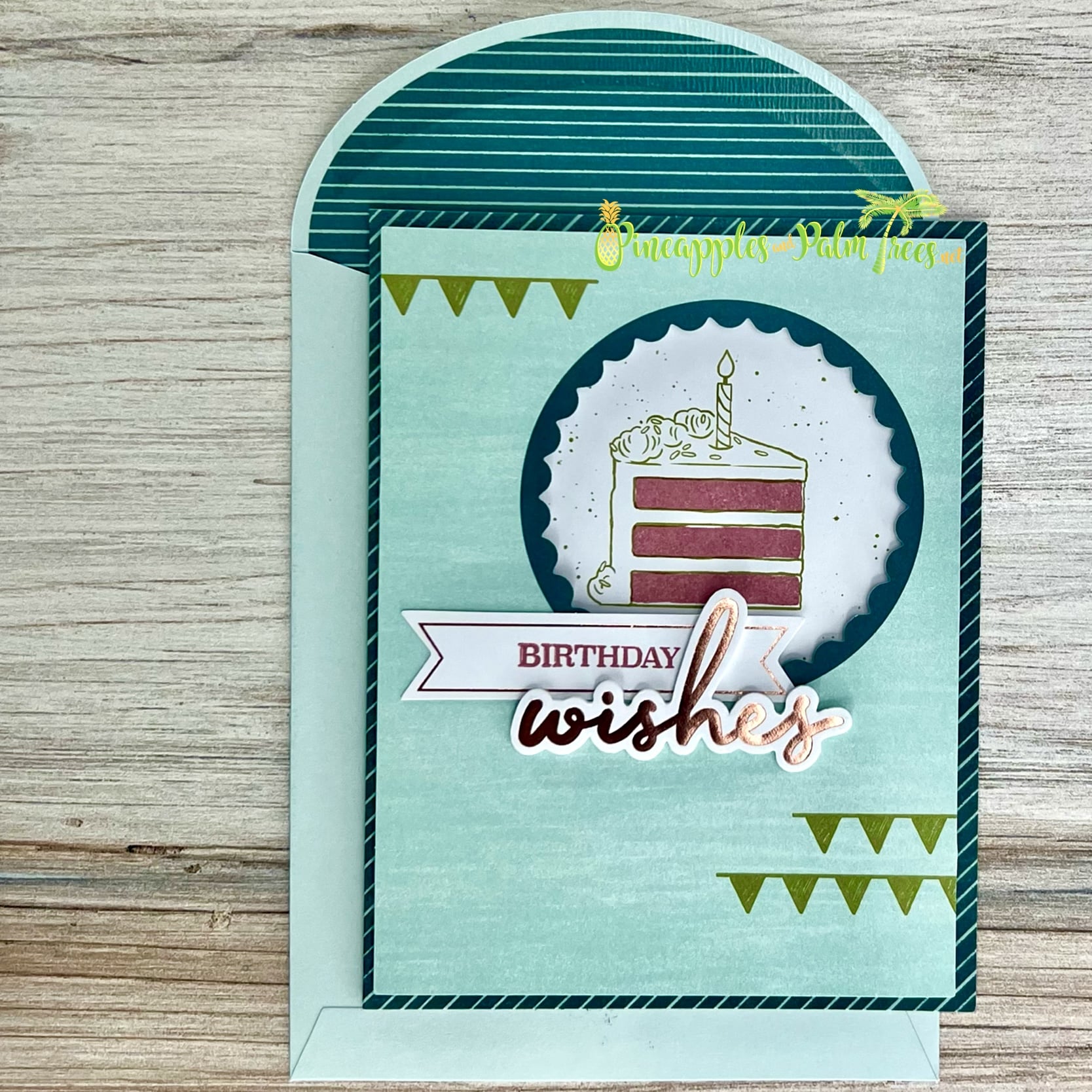 A handmade birthday card with a fun and playful design. The card features a die-cut cake with a candle, surrounded by a scalloped circle. The sentiment "BIRTHDAY wishes" is included on a banner. The card has a teal background with a striped pattern and a matching teal envelope.