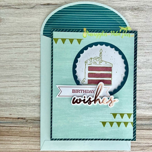 A handmade birthday card with a fun and playful design. The card features a die-cut cake with a candle, surrounded by a scalloped circle. The sentiment "BIRTHDAY wishes" is included on a banner. The card has a teal background with a striped pattern and a matching teal envelope.