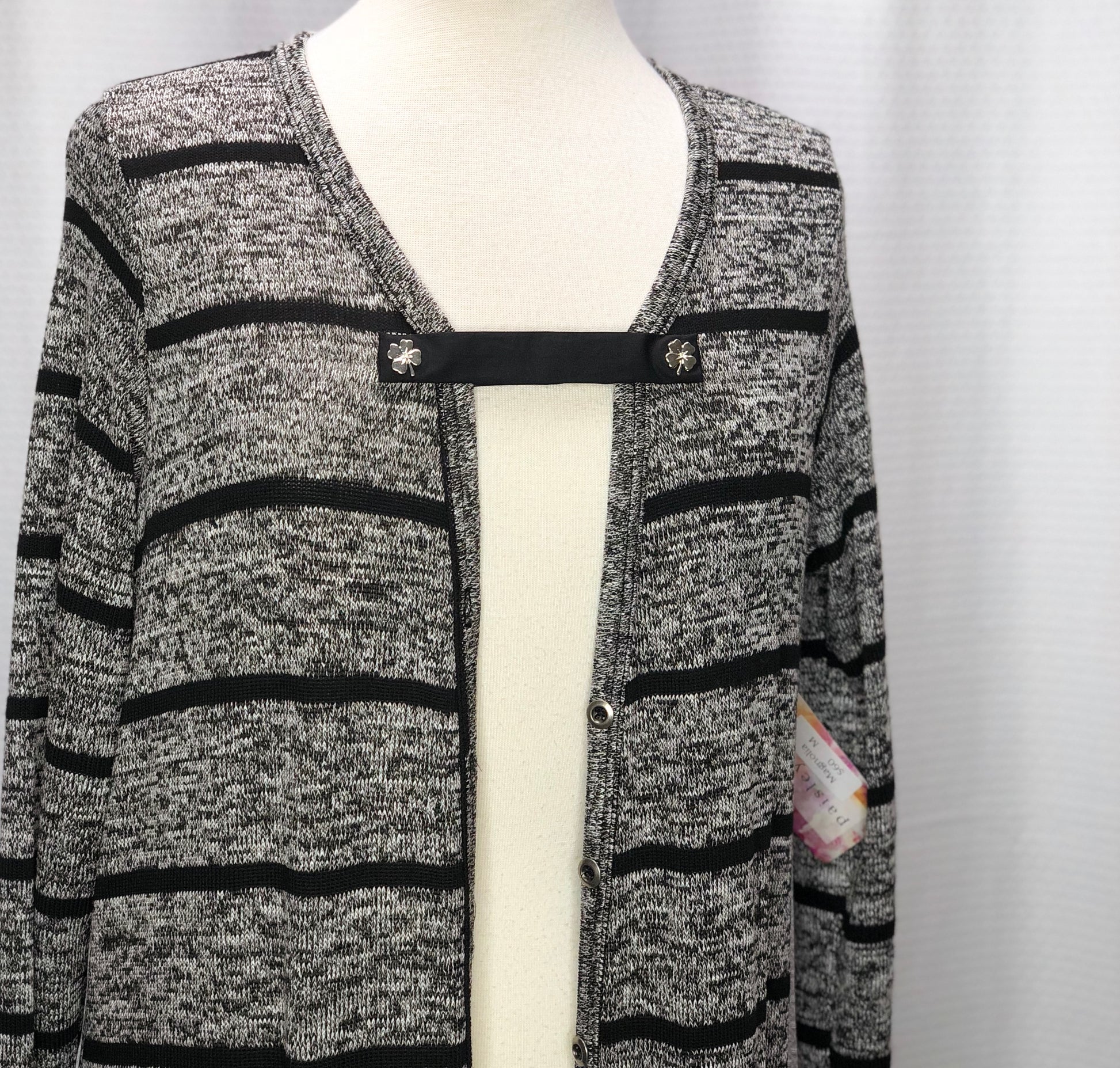 A ladies long gray knitted cardigan sweater with horizontal black stripes, on a fabric mannequin, against a white background.  A black FitClip with 4-leaf clovers on each end are holding the sweater together at the lower portion of the neckline, as a demo example of how to style a FitClip.