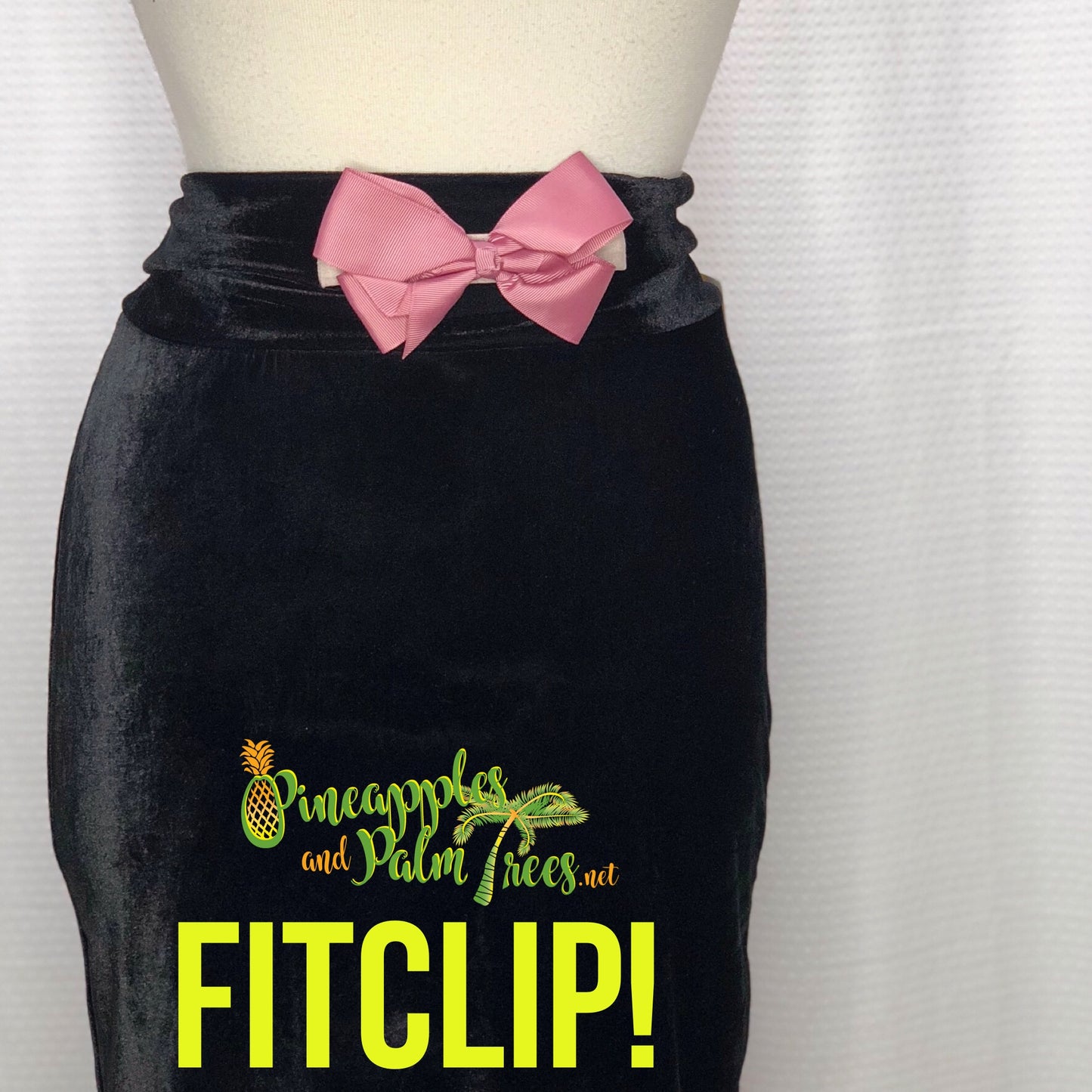 Against a white background, a black mini skirt is displayed on a mannequin.  A dusty rose FitClip with a bow is attached to the front of the skirt, like a belt, as a demo example of how to style a FitClip.  