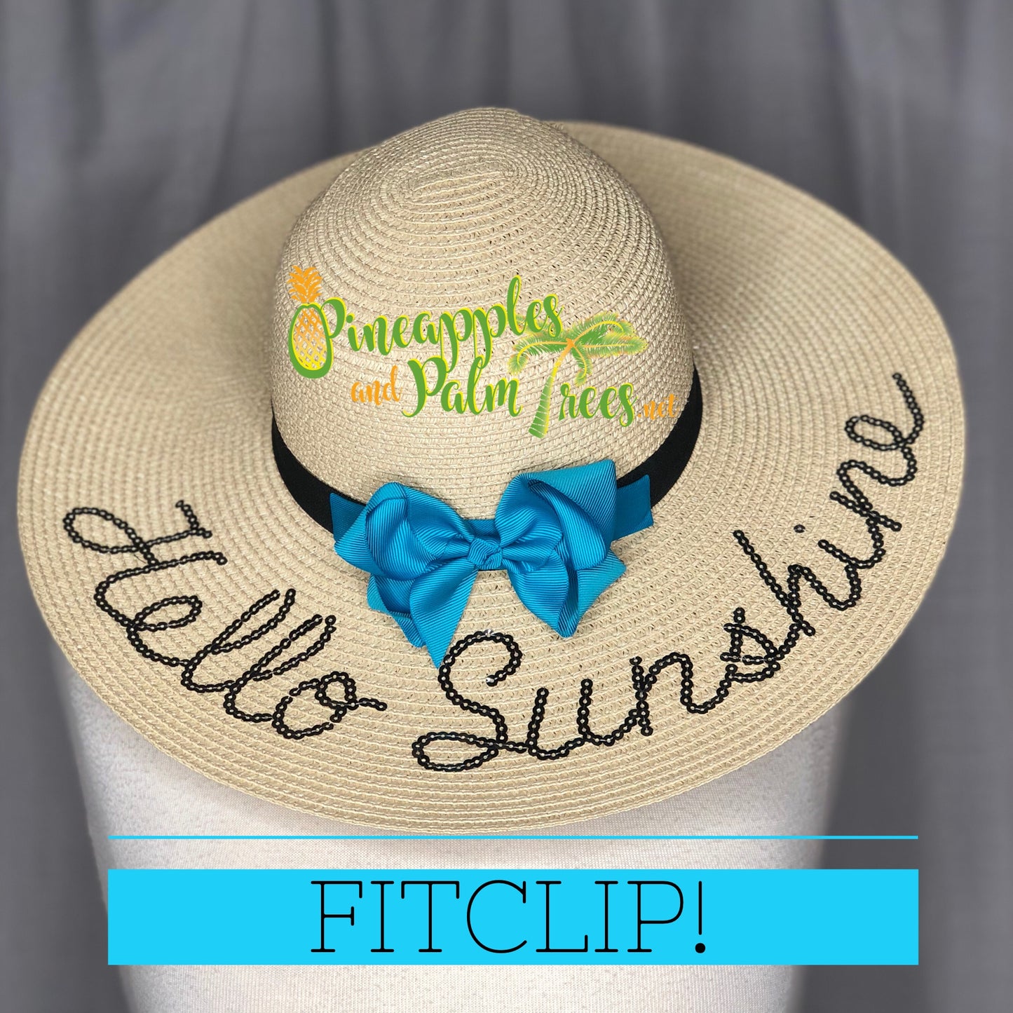 Ladies sun hat that has Hello Sunshine embroidered across the top brim.  An aqua blue FitClip with a bow is attached to the band, as a demo example of how to style a FitClip.  Sun hat is resting on a fabric mannequin with a gray background.