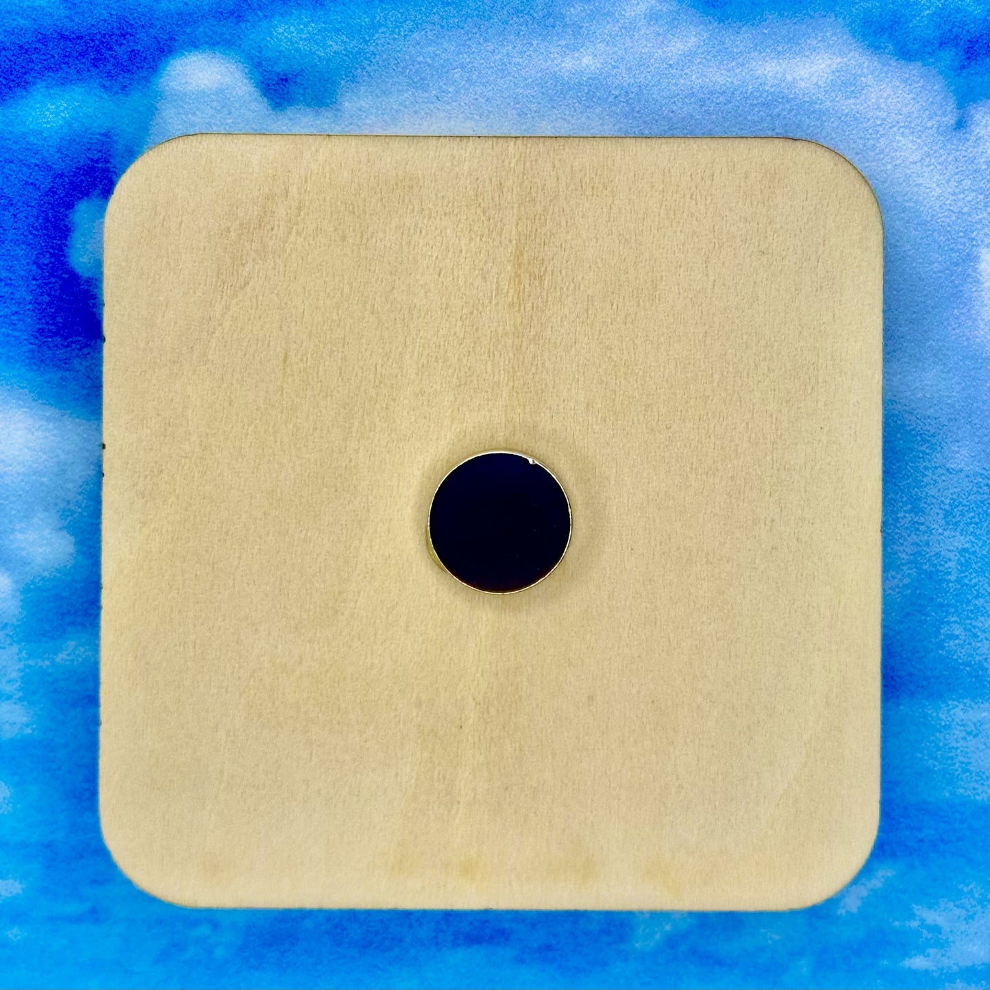 Backside of a 2”x2” wooden square with a magnet in the center. Background is tan/brown granite.