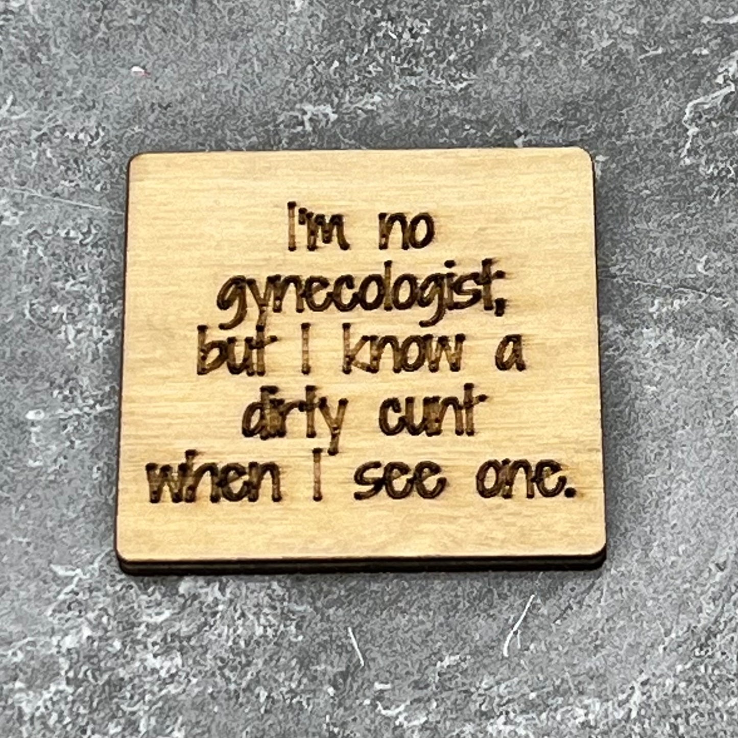 2.5" basewood square with “I’m no gynecologist but I know a dirty cunt when I see one.“ laser engraved text.