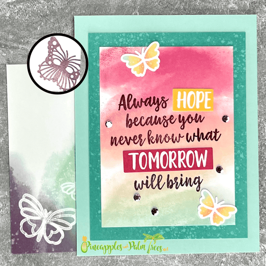 A handmade card with a watercolor background in shades of pink, orange, and yellow. The card features the sentiment "Always HOPE because you never know what TOMORROW will bring" in black script. Two orange, yellow and blue butterflies are die-cut and arranged around the sentiment. Has a matching butterfly stamp inside and has a matching turquoise and purple envelope.