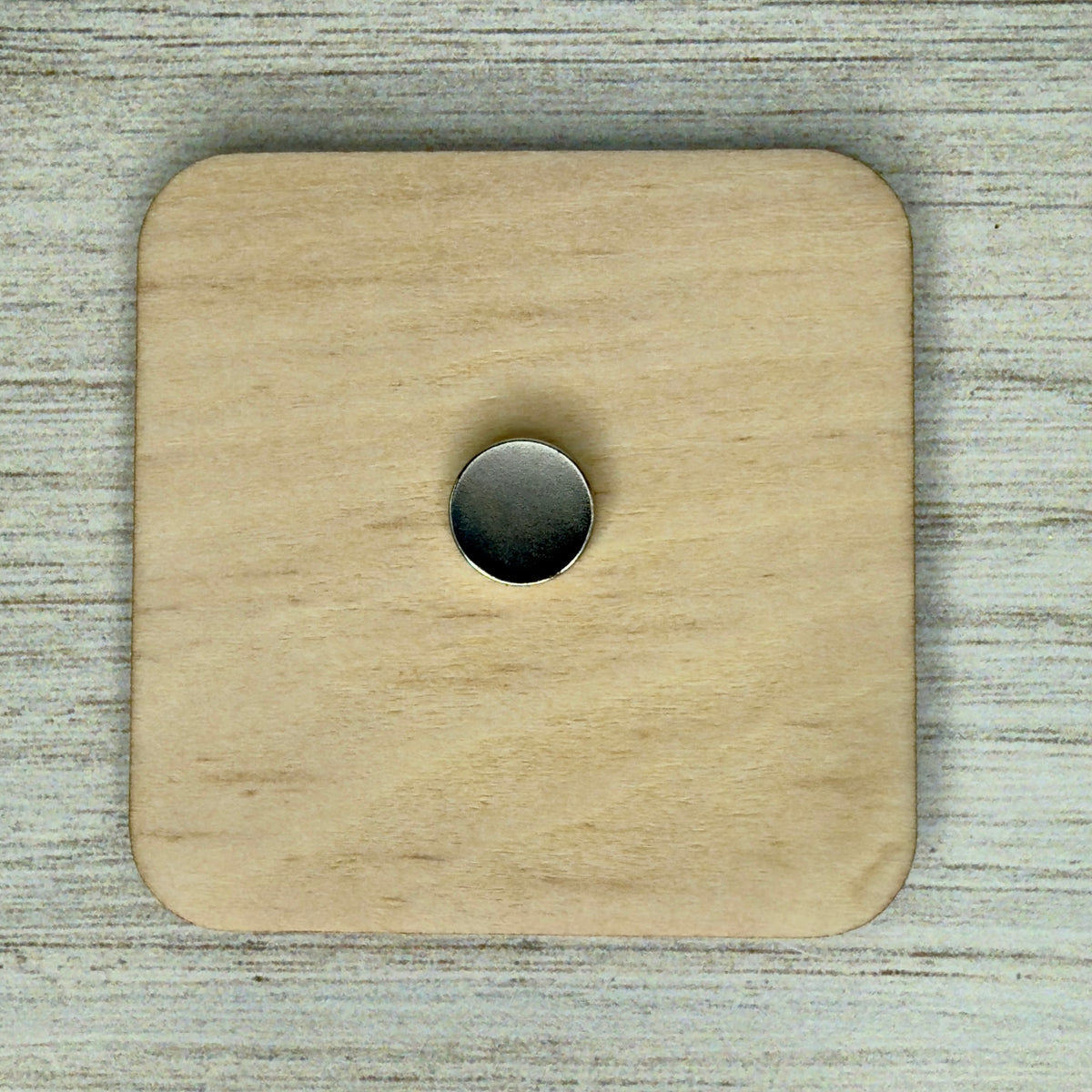 Back view of a laser-cut wooden fridge magnet showing smooth wood grain and a strong round magnet securely attached at the center.
