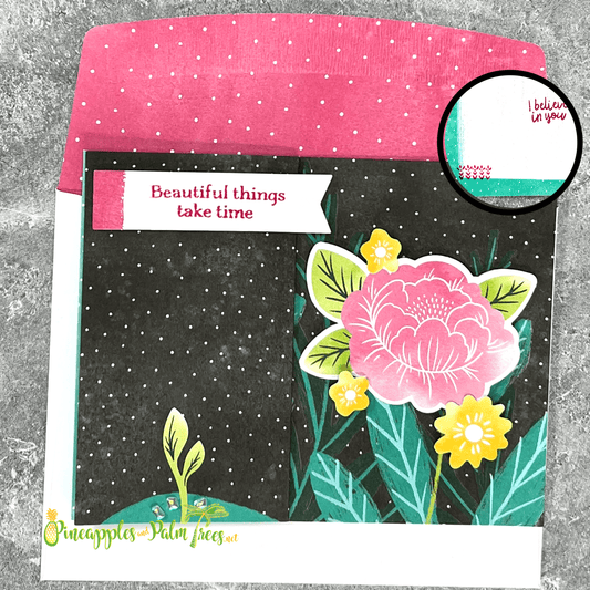 A handmade card with a layered design. The card features a pink peony flower with smaller yellow background flowers. The card has a dark background with white polka dots and a sentiment banner "Beautiful things take time." The card is paired with a white exterior and pink  with a polka-dot pattern inside.
