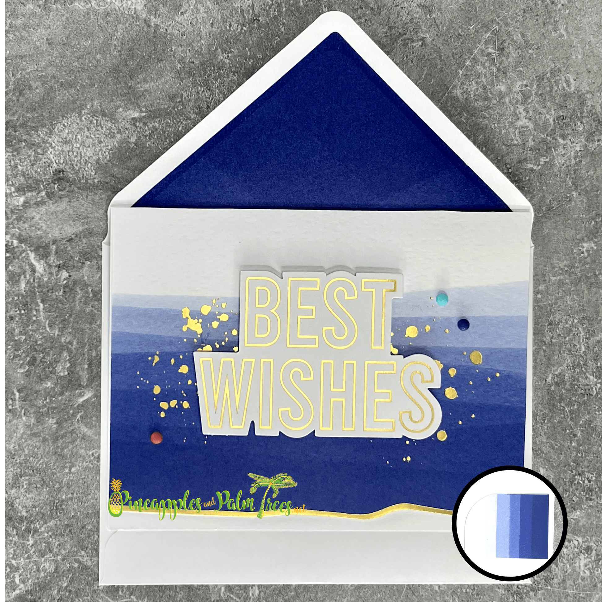 A handmade card with a watercolor background in shades of bold blue. The sentiment "BEST WISHES" is in gold foil and layered over the watercolor. The card is finished with gold glitter splatters and a few colorful dots. Includes a pocket inside for a gift card and has a matching white envelope with a blue lining.
