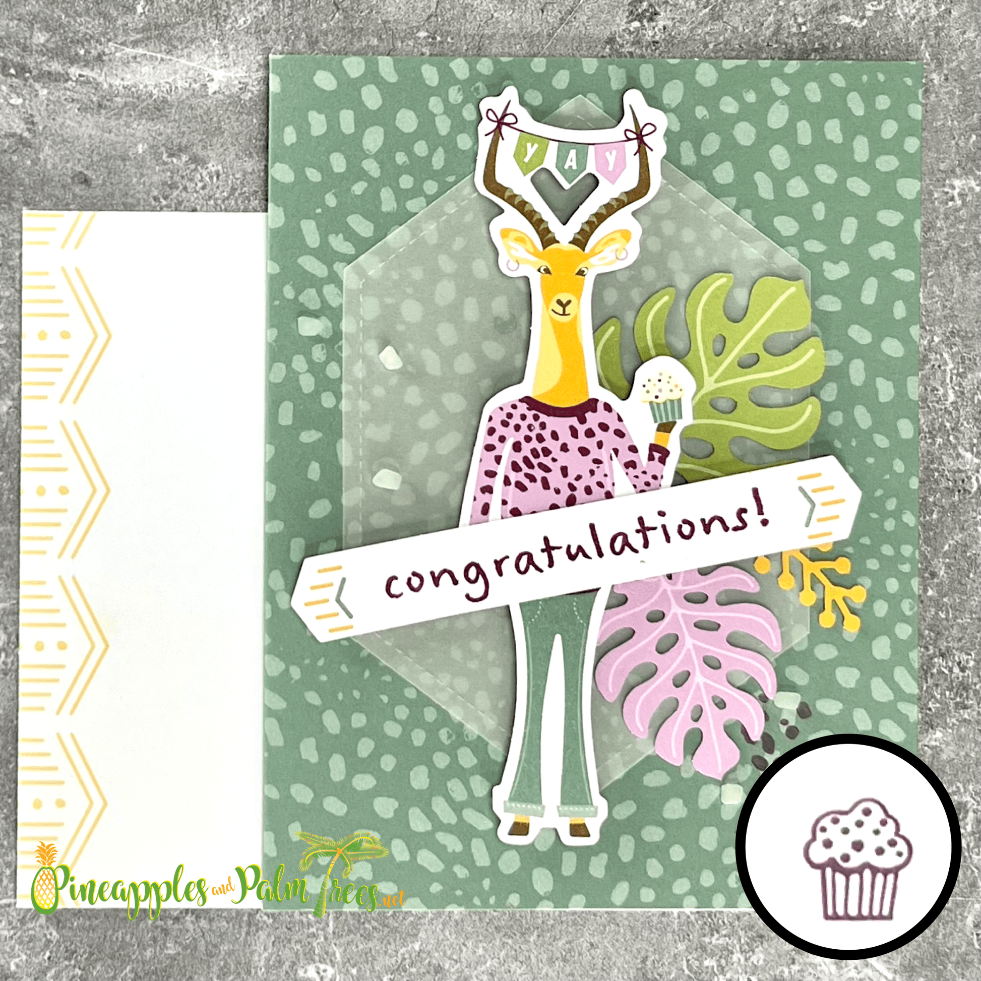 A handmade congratulations card with a safari theme. The card features a giraffe wearing a leopard print sweater and holding a cupcake. The giraffe is surrounded by tropical leaves and a hexagon-shaped frame. A banner at the bottom reads "congratulations!" The card is paired with a white envelope with a tribal pattern.