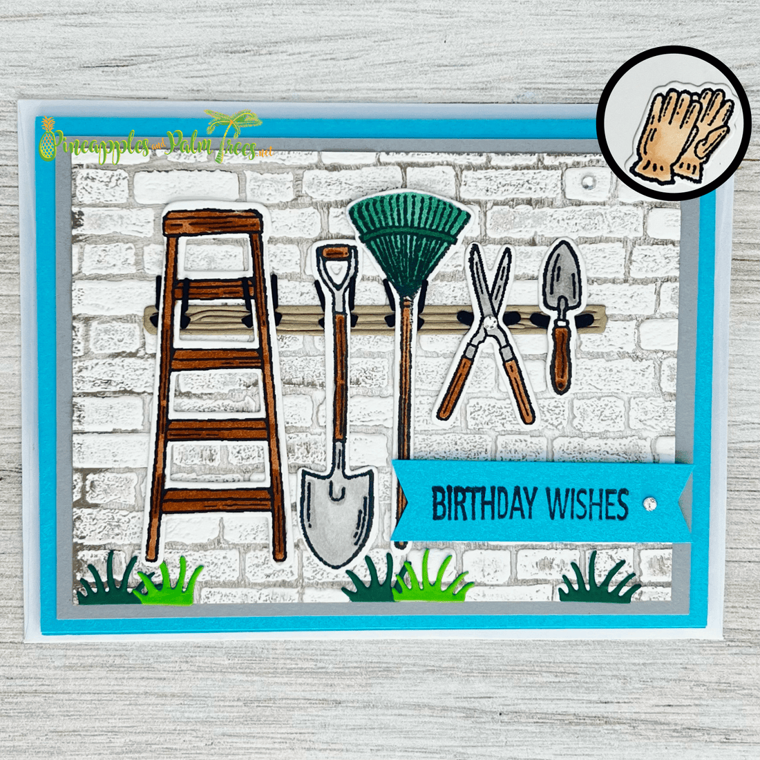 white brick wall with ladder, shovel, drake, shears and trowel attached to wood beam, with grass sprouting at the bottom and blue tag with sentiment 'birthday wishes'.  Inside is a stamp of an orange pair of garden gloves