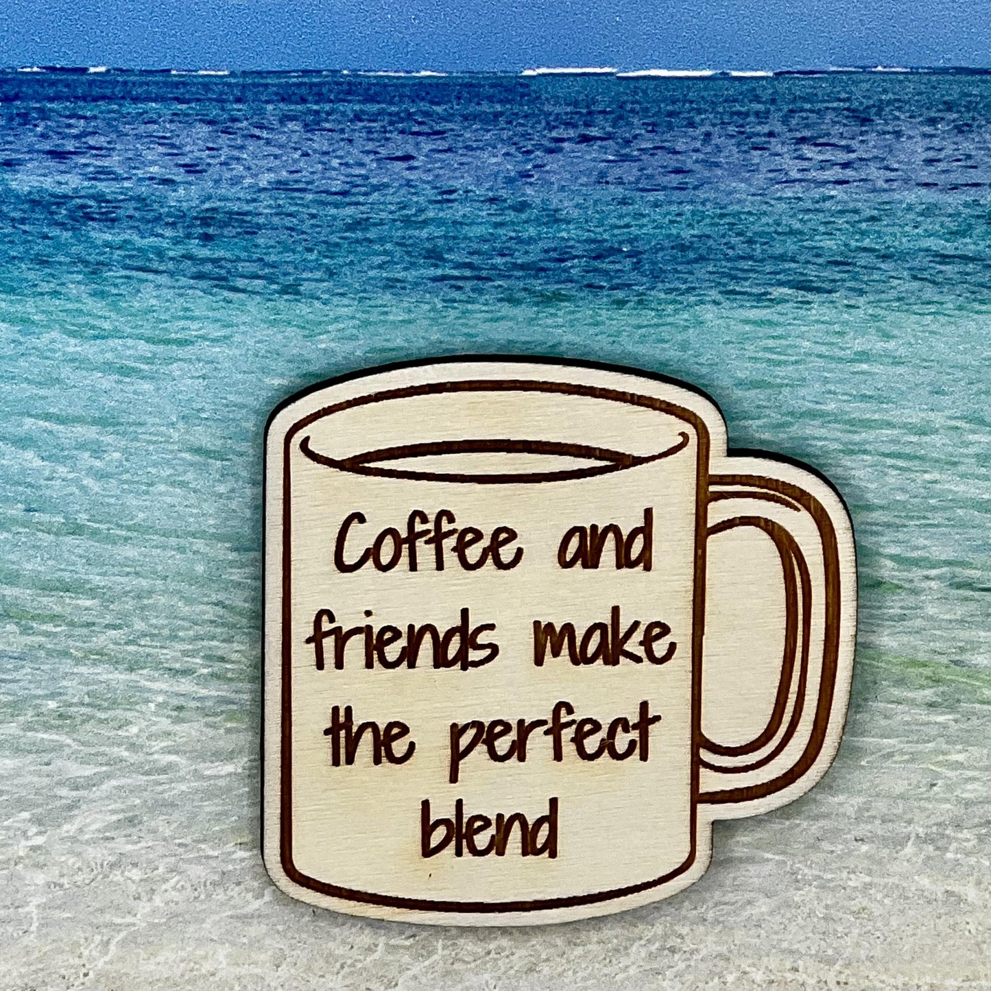 Wood outline of a coffee mug with “Coffee and Friends Make the Perfect Blend“ laser engraved. Background scene is a tropical ocean.