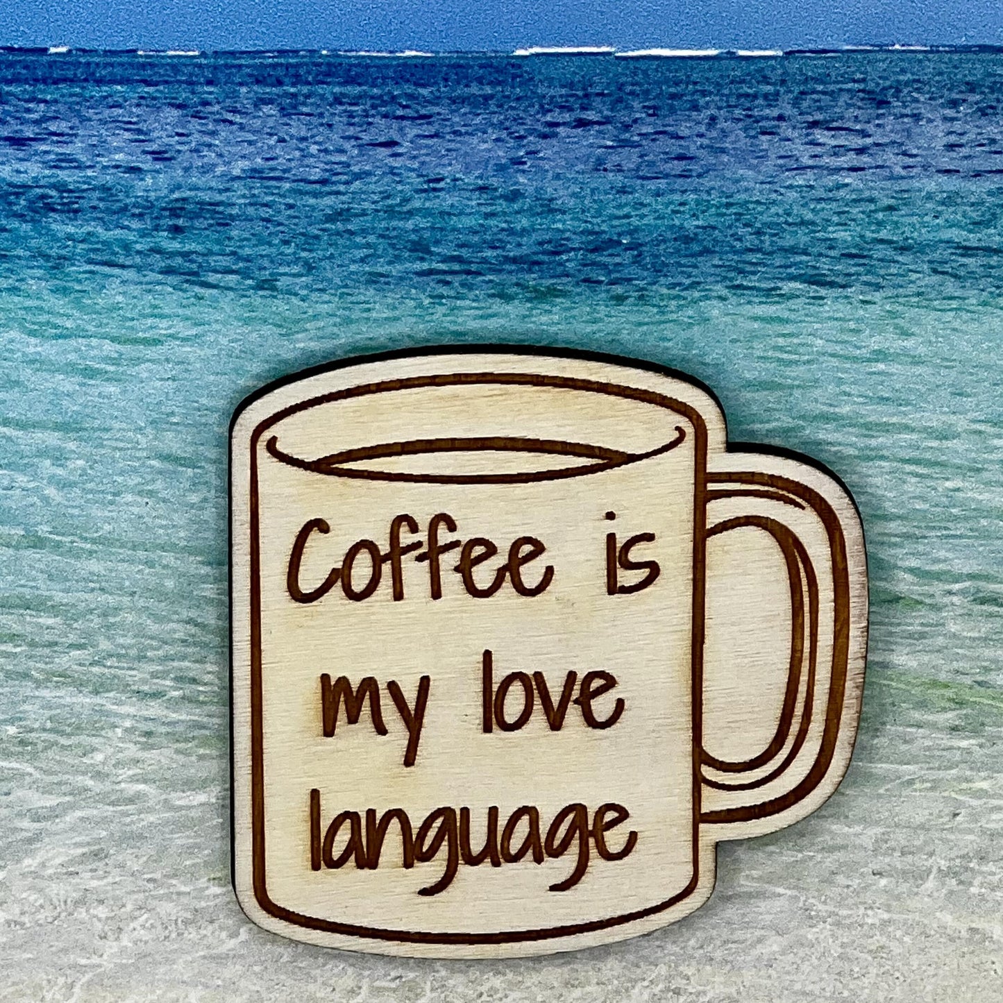 Wood outline of a coffee mug with “Coffee is my Love Language“ laser engraved. Background scene is a tropical ocean.