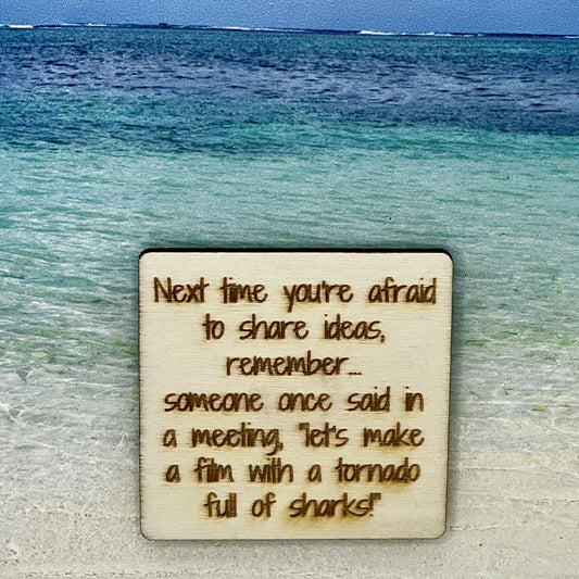 2”x2” wooden square with “Next Time You're Afraid to Share Ideas, Remember... Someone Once Said in a Meeting, "Let's Make a Film With a Tornado Full of Sharks!“ laser engraved. Background scene is a tropical ocean.