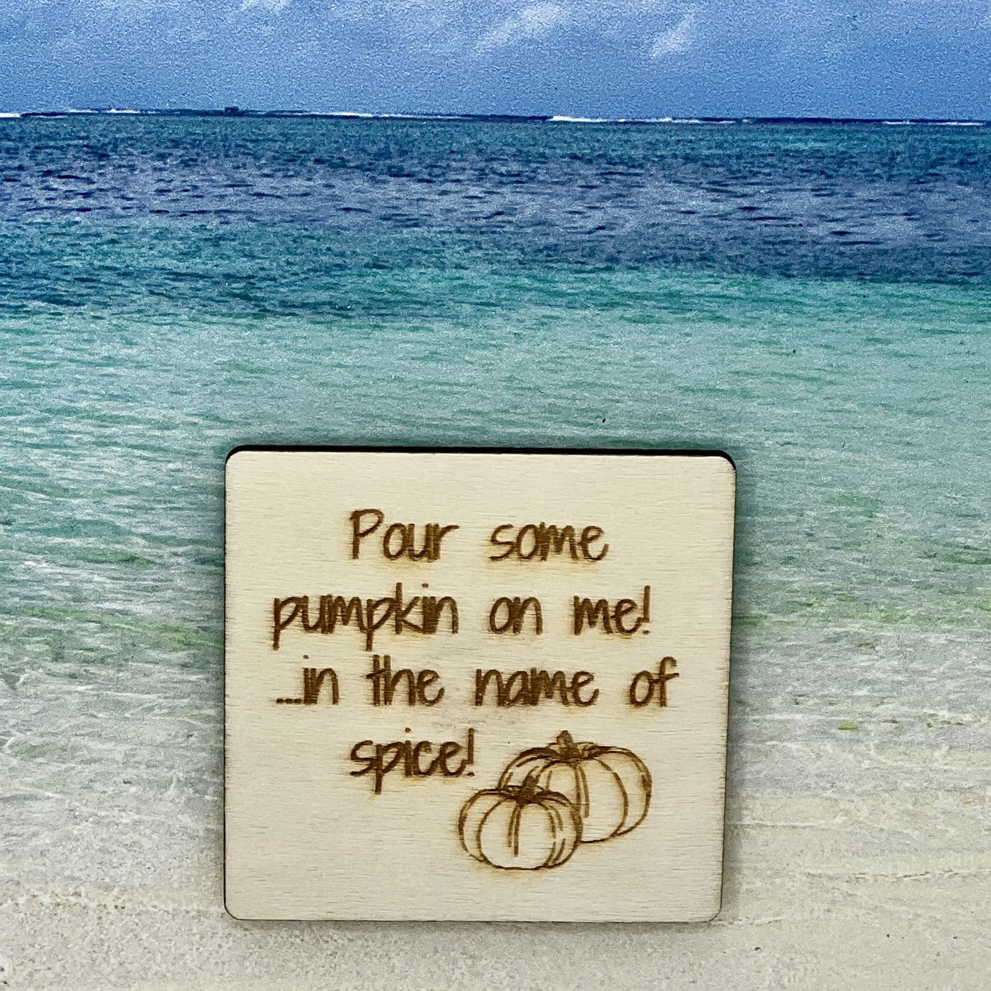 2”x2” wooden square with “Pour Some Pumpkin on Me! ...in the Name of Spice!“ and two pumpkins, laser engraved. Background scene is a tropical ocean.