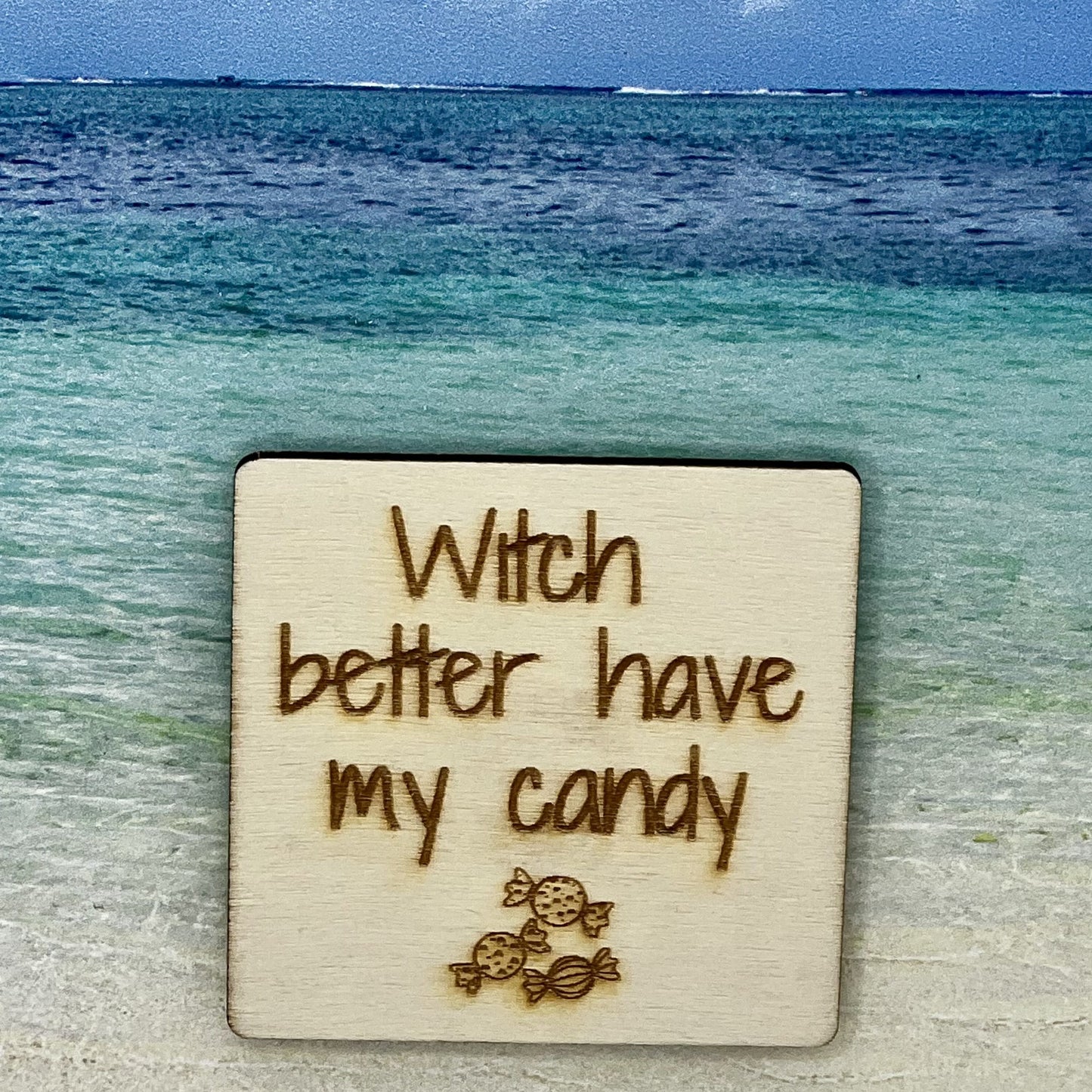 2”x2” wooden square with “Witch Better Have my Candy“ and 3 pieces of wrapped candy, laser engraved. Background scene is a tropical ocean.