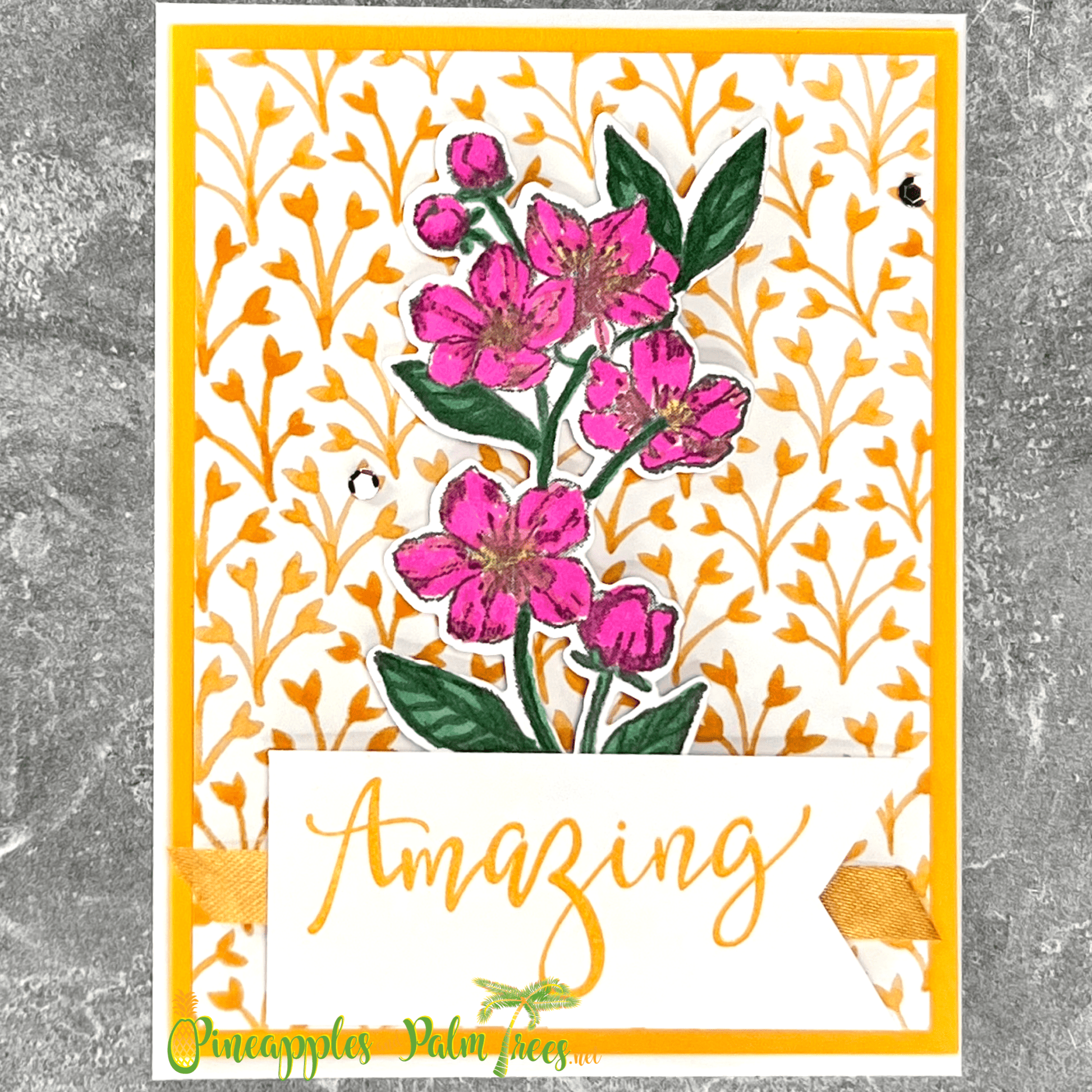 A handmade card featuring a beautiful pink floral arrangement with green leaves. The flowers are accented with gold glitter. The card has a yellow background with a delicate pattern of branches. A banner at the bottom reads "Amazing" in gold script and includes a white envelope.