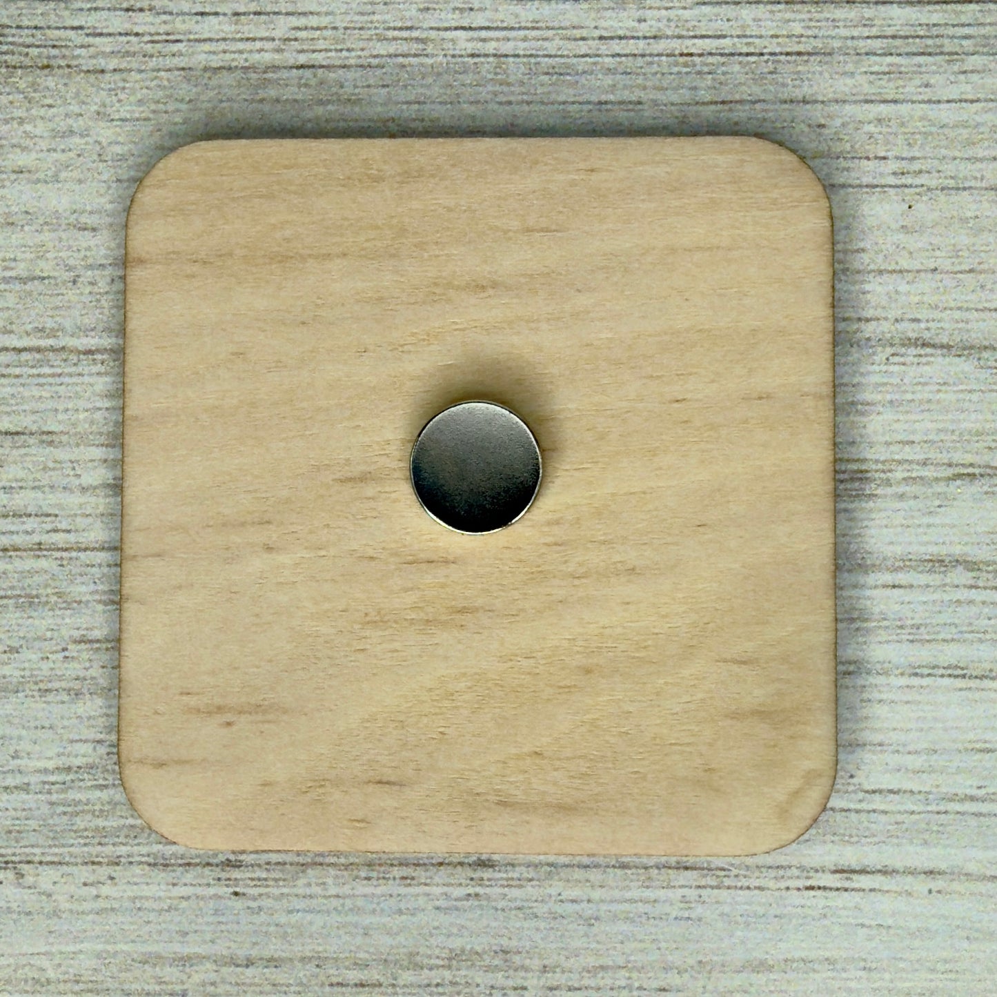 Back view of a laser-cut wooden fridge magnet showing smooth wood grain and a strong round magnet securely attached at the center.
