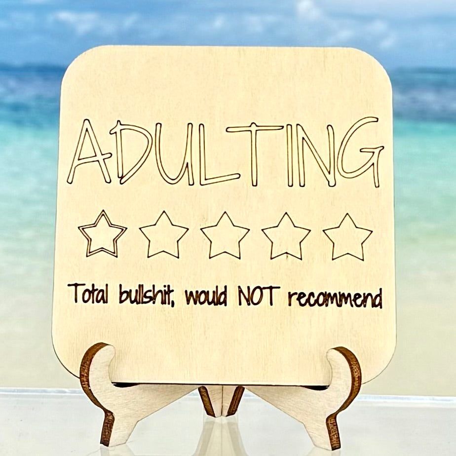 Wooden‑style fridge magnet: ‘Adulting — 1 star. Total bullshit, would not recommend’ — sarcastic adult life quote.
