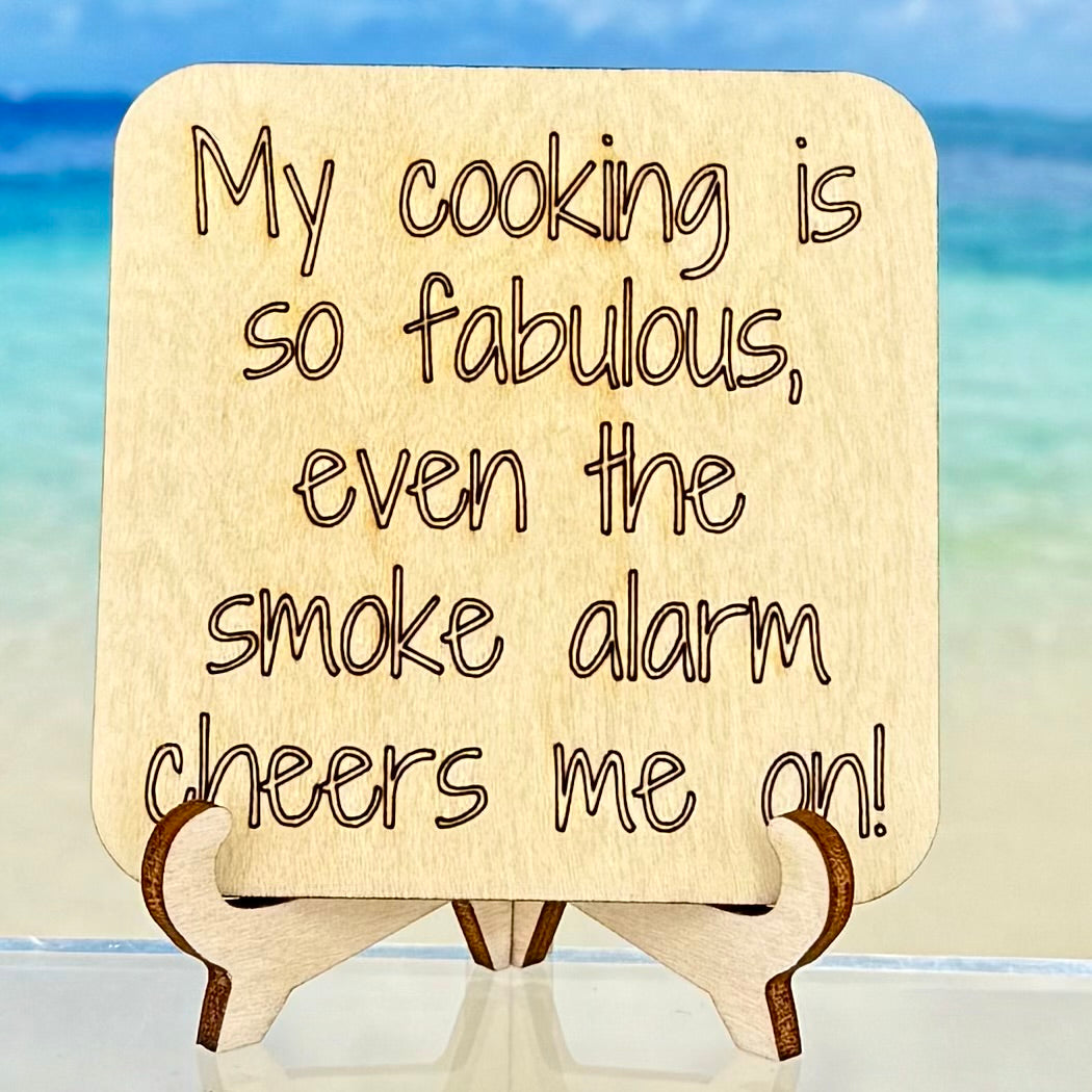 Laser-cut wooden fridge magnet engraved with the quote ‘My cooking is so fabulous, even the smoke alarm cheers me on!’ — humorous kitchen décor piece from Pineapples & Palm Trees.