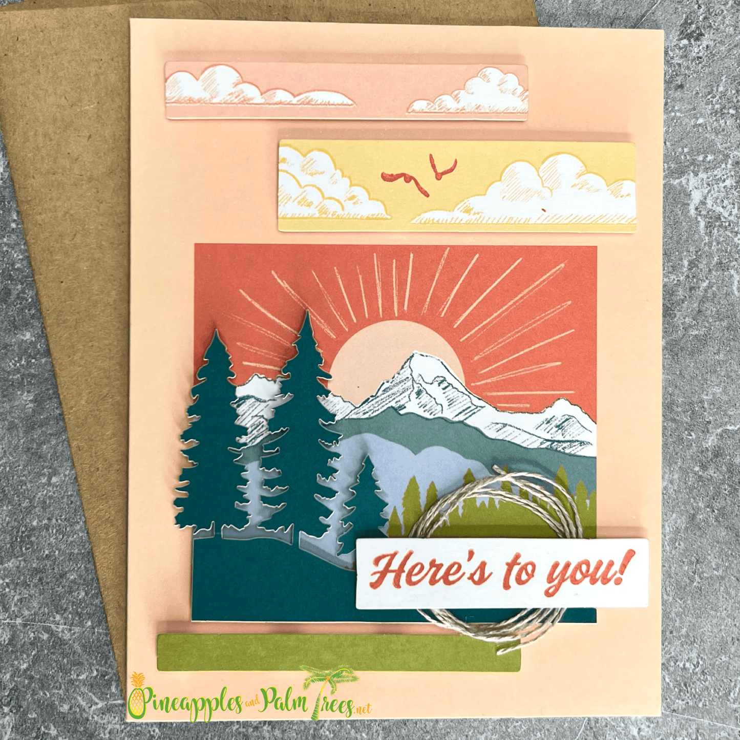 Greeting card with the message ‘Here’s to you,’ illustrated with a sun rising over stylized mountain peaks, shown with its matching envelope — warm and uplifting design.