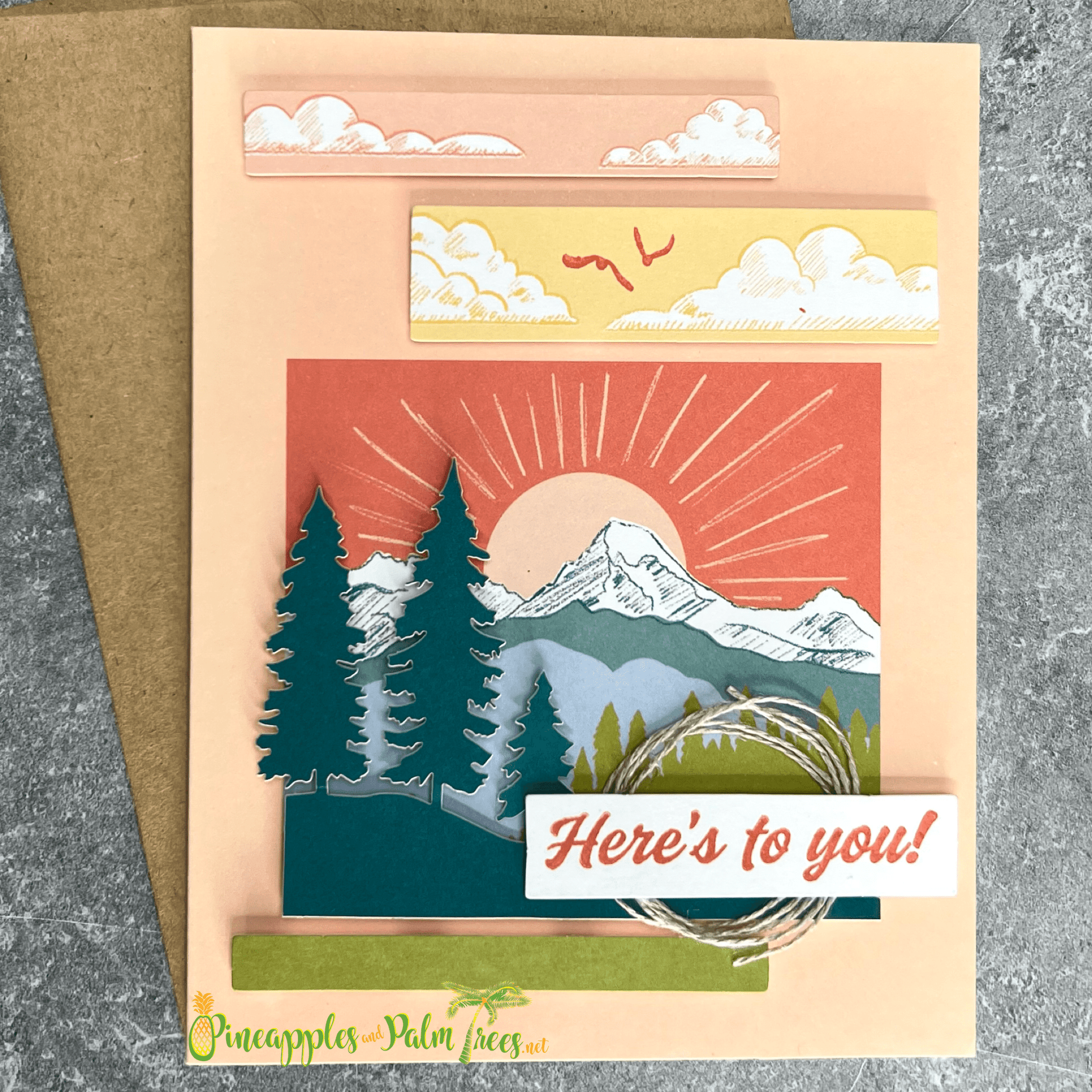 Greeting card with the message ‘Here’s to you,’ illustrated with a sun rising over stylized mountain peaks, shown with its matching envelope — warm and uplifting design.