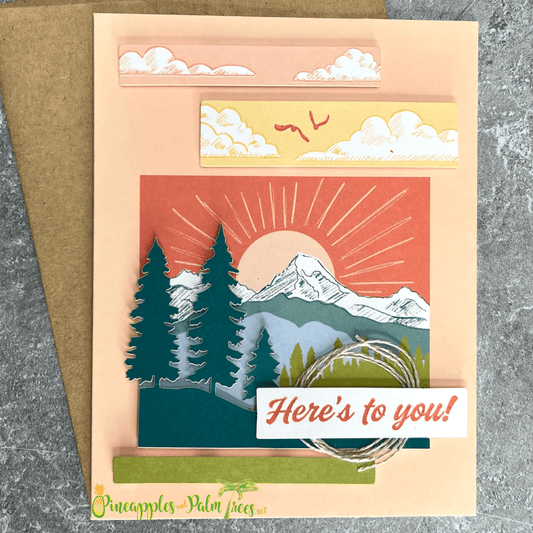 Greeting card with the message ‘Here’s to you,’ illustrated with a sun rising over stylized mountain peaks, shown with its matching envelope — warm and uplifting design.