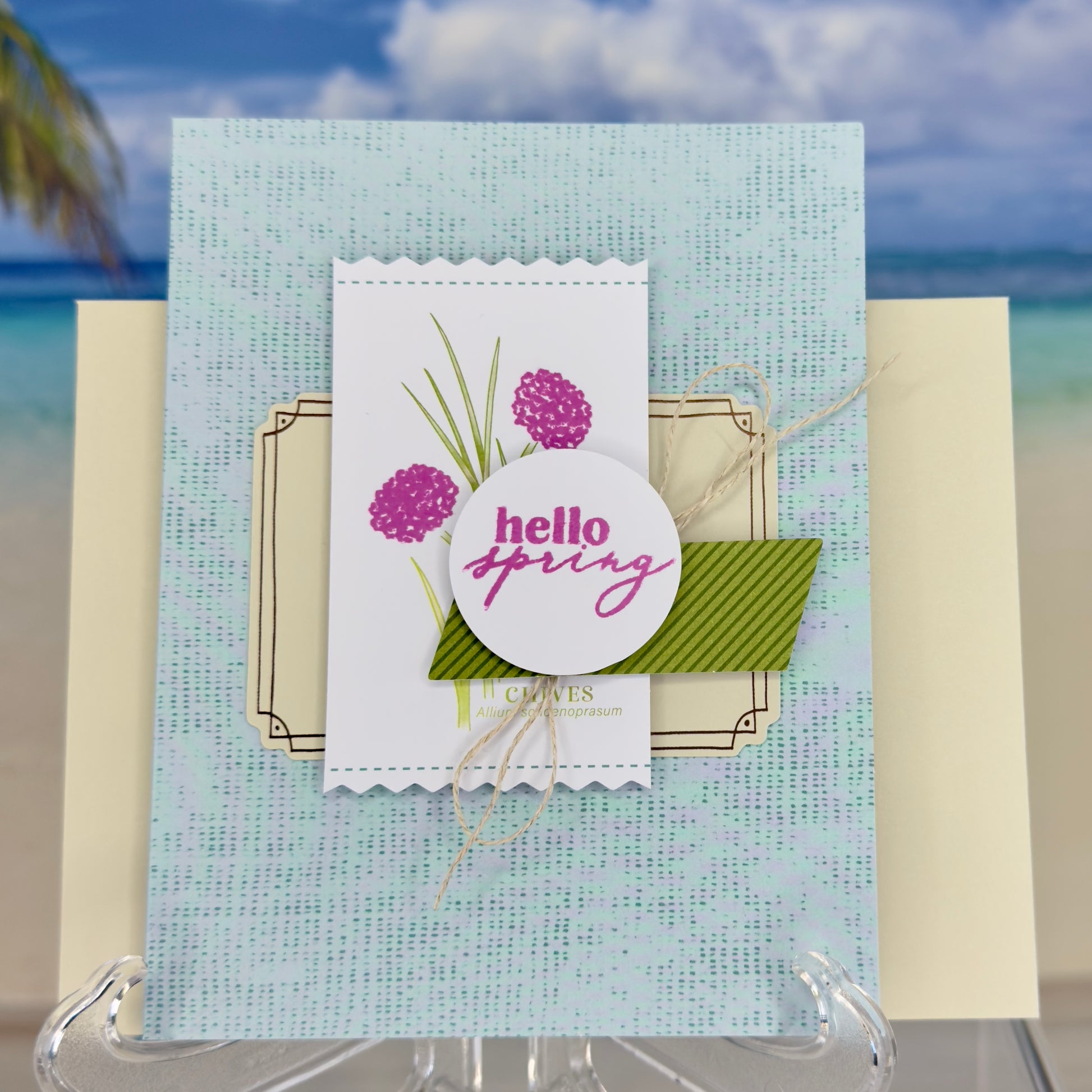 Greeting card with the words ‘Hello Spring’ surrounded by green chive stems and simple floral accents, shown with its matching envelope — light, fresh, and handcrafted.