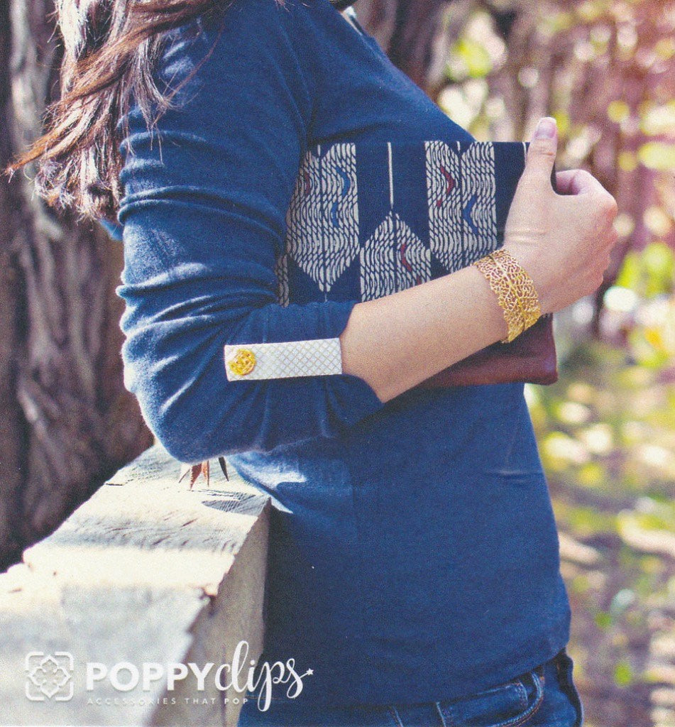 Front of packaging, showing a female in a blue, long sleeve shirt, with a white Poppyclip with gold medallion holding up her sleeve right – very cute! And the logo, ‘Poppyclips’ accessories that pop in the bottom right-hand corner.